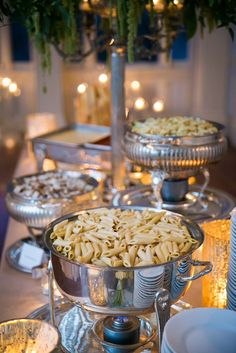 an assortment of food is displayed on a table with silver dishes and candles in the background