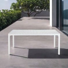 a white table sitting on top of a cement floor next to a tree and bushes