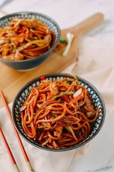 two bowls filled with noodles and vegetables next to chopsticks