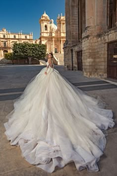 a woman in a white wedding dress standing on the street with an old building behind her