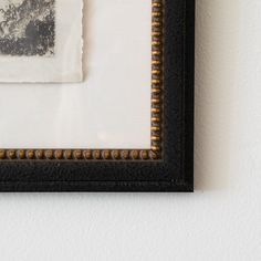 an old photo hanging on the wall in a black frame with gold bead trim