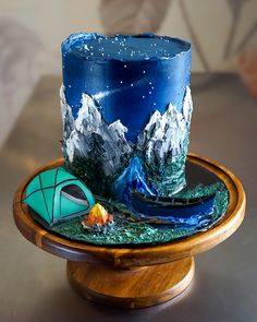 a blue candle with mountains in the background and a tent on a wooden stand next to it