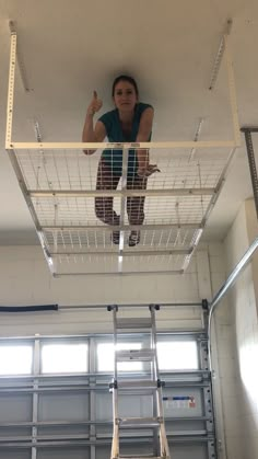 a woman standing on top of a metal cage next to a ladder in a garage