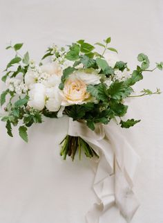 a bridal bouquet with white flowers and greenery is tied up against a wall