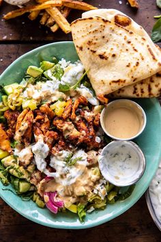 a salad with chicken, lettuce and dressing on a plate next to pita bread