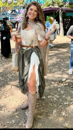 a woman dressed in costume holding a drink and cell phone while standing on dirt ground