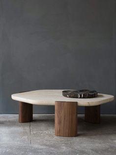 an oval table with two wooden legs and a black object on the top, in front of a gray wall