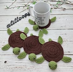 two crocheted turtle coasters sitting next to a coffee cup