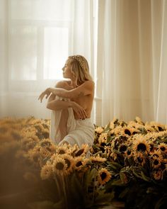 a naked woman sitting on top of a bed of sunflowers next to a window