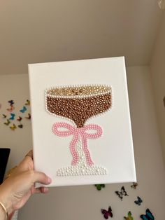 someone is holding up a painting with pearls on it and a pink bow around the edge