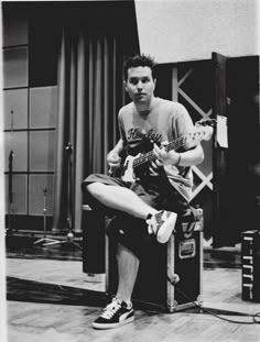 a man sitting on top of a chair playing an electric guitar in front of a microphone