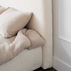 a white bed with two pillows on top of it next to a wall and window