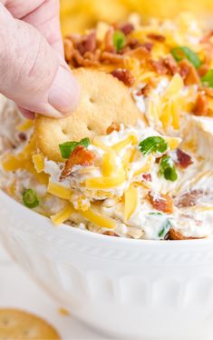 a hand dipping crackers into a bowl of loaded potato salad