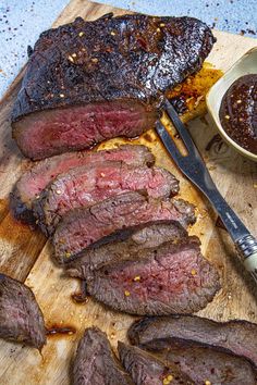 sliced steak on cutting board with knife and fork next to bowl of bbq sauce