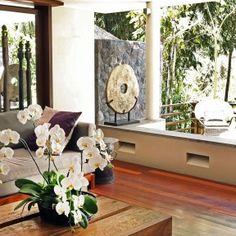 a living room filled with furniture and flowers on top of a wooden table in front of a window