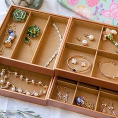 an assortment of jewelry sits in a box on a table next to a flowery pillow