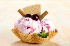 two scoops of ice cream with cherries and mint leaves in waffle cones