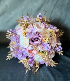 a bridal bouquet with purple and white flowers on a black cloth covered tablecloth