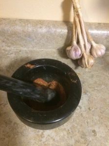 two garlic sticks sticking out of a black bowl on a counter next to some cloves