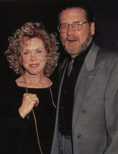 a man and woman standing next to each other in front of a dark background,