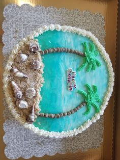 there is a cake that has been decorated with shells and palm trees on the beach