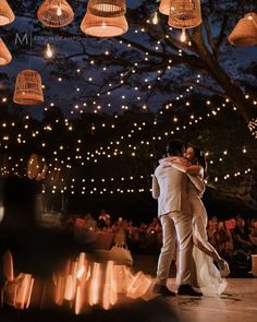 a bride and groom sharing their first dance under hanging lights at night with guests watching