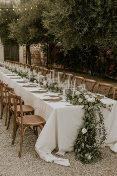 a long table with white linens and greenery is set up for an outdoor dinner