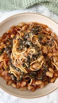 a bowl filled with pasta and spinach on top of a marble countertop next to a green towel