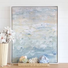 a painting and vase with flowers on a wooden table in front of a white wall