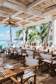 an outdoor dining area with tables, chairs and umbrellas overlooking the ocean on a sunny day