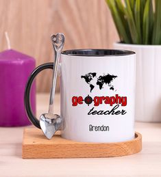 a white coffee mug with the words go graphy teacher on it next to a spoon