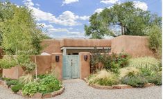 an adobe - style home in the desert surrounded by greenery and shrubs, with a blue door