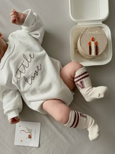 a baby laying on its back next to a box with a cake and socks in it