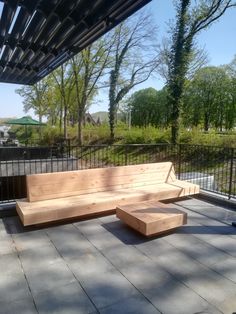 a wooden bench sitting on top of a cement floor next to a metal fence with trees in the background