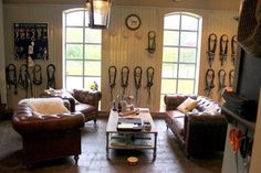 a living room filled with brown furniture and lots of clutter on the wall next to two large windows