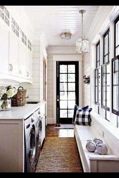 a long narrow hallway with white cabinets and black doors is flanked by a washer and dryer