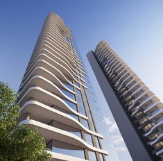 two tall buildings next to each other with trees in the foreground and blue sky behind them