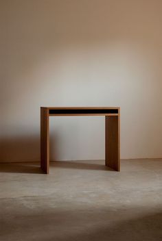 a wooden table sitting on top of a cement floor next to a white wall in an empty room