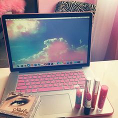 an open laptop computer sitting on top of a desk next to lipstick and makeup products