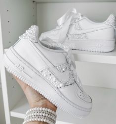 a woman's hand holding up a white nike air force sneakers with pearls on them