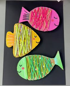 two fish made out of paper sitting on top of a piece of black paper next to each other