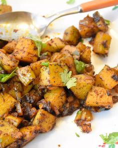 a white plate topped with cooked potatoes and garnished with parsley next to a spoon