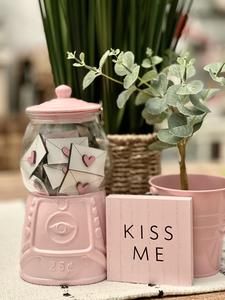 a pink vase with some flowers in it next to a sign that says kiss me