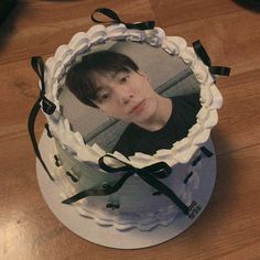 a birthday cake with a photo on the top and black ribbon around the bottom, sitting on a wooden table