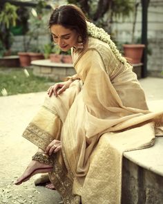 a woman sitting on top of a stone bench wearing a white and gold sari