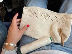 a woman's hand holding a white purse with crochet and knitting needles