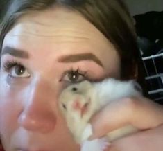 a woman holding a small animal up to her face and looking at the camera with an intense look on her face