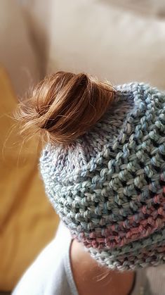 a close up of a person wearing a knitted hat with a messy top knot