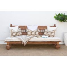 a wooden bench with pillows on it in front of a white wall and potted plant