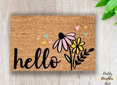 a door mat with the word hello written on it and flowers in front of it